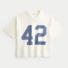 Raskas, väljä, lyhyt varsity-grafiikka-jalkapallopaita Raskas, väljä, lyhyt varsity-grafiikka-jalkapallopaita